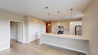 Located at 1208 W Maumee St in Angola, Indiana, this thoughtfully designed 2-bedroom, 2-bathroom unit offers a clean, modern aesthetic throughout its well-utilized single-floor layout. Light hardwood flooring flows continuously through every room, complementing the warm neutral tones on the walls and trim.

The open-concept kitchen is a standout feature, anchored by a generous white countertop island with a built-in sink and seating overhang. Pendant lights with brass accents hang above, adding a refined touch. Cream-toned flat-panel cabinetry lines the walls, complemented by a tile backsplash and a full suite of stainless steel appliances, including a range, microwave, refrigerator, and dishwasher. An adjacent window brings in natural light.

The living area is bright and airy, with large windows and a glass-paned entry door that frame outdoor views and invite abundant natural light. The primary bedroom is spacious and connects directly to an en-suite bathroom, which features a white vanity, undermount sink, and mirrored medicine cabinet. A walk-in closet with wire shelving provides ample storage. The second bedroom includes sliding panel doors concealing a built-in closet. A second full bathroom with matching finishes serves the remaining rooms. A hallway ties the layout together efficiently.
