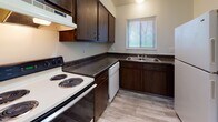 This single-floor unit at 2446 Wyoming St in Dayton, Ohio offers a practical and comfortable layout designed for everyday living. The kitchen is well-appointed with dark espresso-stained cabinetry, dark granite-style countertops, a coil-burner electric range, a built-in dishwasher, a stainless steel sink, and an overhead ventilation hood. A window with blinds allows natural light to brighten the space. Wood-look vinyl flooring runs throughout the kitchen, adding a clean, modern touch. The living area is generously sized, featuring soft wall-to-wall carpeting, a ceiling fan, and a large sliding glass door dressed with vertical blinds that opens to an outdoor view, filling the room with abundant natural light. The bedroom is equally spacious, also carpeted, with its own set of floor-to-ceiling vertical blinds covering a large window that invites plenty of daylight. An additional carpeted room provides flexible space suitable for a bedroom or office. The bathroom is neatly finished with wood-look flooring, a full tub-shower combination with tiled surround, a toilet, and a white vanity with storage below. Neutral wall tones and consistent flooring choices throughout give the unit a cohesive and move-in-ready feel.