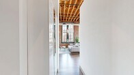 Located at 1531 S Eighth St in St. Louis' historic Soulard neighborhood, this one-bedroom, two-bathroom loft blends industrial character with modern elegance. Soaring ceilings with exposed wooden beam rafters and dramatic floor-to-ceiling steel-framed windows define the open living area, which is bathed in natural light and anchored by a striking crystal chandelier. The exposed red brick walls add warmth and texture throughout, creating a bold architectural backdrop. Hardwood floors run through the living space, which features a cozy fireplace and a seamless flow into the dining area.

The open kitchen is well-appointed with light wood cabinetry, granite countertops, a peninsula breakfast bar with seating, industrial pendant lighting, and open pipe shelving. Tall windows in the kitchen provide abundant natural light and views of the surrounding cityscape.

The spacious primary bedroom continues the loft's signature aesthetic with exposed brick, soaring ceilings, a crystal chandelier, and large windows. The room offers generous space and a sense of airy grandeur. Two bathrooms serve the unit — one featuring a double-sink vanity with granite countertops and wood cabinetry, and the other a full tub/shower combination with granite counters. A connecting hallway completes the thoughtfully designed floor plan.