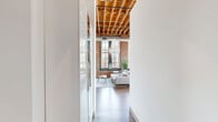 Located at 1531 S Eighth St in St. Louis' historic Soulard neighborhood, this one-bedroom, two-bathroom loft blends industrial character with modern elegance. Soaring ceilings with exposed wooden beam rafters and dramatic floor-to-ceiling steel-framed windows define the open living area, which is bathed in natural light and anchored by a striking crystal chandelier. The exposed red brick walls add warmth and texture throughout, creating a bold architectural backdrop. Hardwood floors run through the living space, which features a cozy fireplace and a seamless flow into the dining area.

The open kitchen is well-appointed with light wood cabinetry, granite countertops, a peninsula breakfast bar with seating, industrial pendant lighting, and open pipe shelving. Tall windows in the kitchen provide abundant natural light and views of the surrounding cityscape.

The spacious primary bedroom continues the loft's signature aesthetic with exposed brick, soaring ceilings, a crystal chandelier, and large windows. The room offers generous space and a sense of airy grandeur. Two bathrooms serve the unit — one featuring a double-sink vanity with granite countertops and wood cabinetry, and the other a full tub/shower combination with granite counters. A connecting hallway completes the thoughtfully designed floor plan.