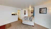 This two-floor residence offers a thoughtfully arranged layout designed for comfortable everyday living. The main living area greets you with warm, neutral-toned carpeting, a ceiling fan, and a tile-surround fireplace that serves as a natural focal point. A sliding glass door dressed with vertical blinds and draped curtains allows natural light to fill the space, while a compact dining area provides a dedicated spot for meals. The kitchen is efficiently designed in a galley style, featuring white cabinetry, light countertops, parquet-style flooring, and black appliances including a refrigerator and range. A pass-through window connects the kitchen to the living area, enhancing the open feel. The primary bedroom is generously proportioned, offering direct access to a private balcony through a sliding glass door, complemented by additional window views. The second bedroom is equally comfortable, featuring carpet, natural light, and ample wall space. A full bathroom includes a shower-tub combination, a single vanity with mirror, and parquet-style flooring. A carpeted staircase connects the two levels, completing this functional and well-maintained multi-level home.