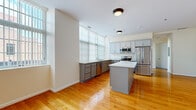 Located at 25 Bittner St in Rochester, NY, this single-floor, 3-bedroom, 2-bathroom residence offers a thoughtfully designed layout that balances comfort and functionality. The open-concept kitchen and living area serves as the heart of the home, showcasing gleaming hardwood floors, crisp white walls, and large windows with vertical blinds that flood the space with natural light. The kitchen is well-equipped with gray cabinetry, stainless steel appliances including a refrigerator, range, and microwave, a central island with a light stone countertop, and a double sink positioned beneath the windows. The generously sized primary bedroom provides ample space and is bathed in natural light from oversized windows. The additional bedrooms feature plush carpeting and large windows with urban views of the surrounding Rochester cityscape. Both bathrooms are finished with neutral tile flooring and tiled tub-shower combinations. A dedicated in-unit laundry room with side-by-side washer and dryer adds everyday convenience. The hallway connects all rooms seamlessly, completing this clean, modern, and move-in-ready urban residence.