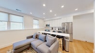 This thoughtfully designed single-floor unit offers four bedrooms and four bathrooms within a compact, efficiently organized layout. The open-concept kitchen and living area serves as the heart of the space, where crisp white cabinetry, white subway tile backsplash, and stainless steel appliances — including a French door refrigerator, electric range, and over-the-range microwave — create a clean, contemporary kitchen. A white waterfall-edge island with barstool seating doubles as a dining area, flowing seamlessly into the living room. The living area features light hardwood flooring, recessed lighting, a wall-mounted flat-screen TV, and windows that allow natural light to filter in. Each of the four bedrooms maintains the same bright, minimalist aesthetic with white walls, light hardwood floors, and built-in closets with double doors accented by matte black hardware. The four bathrooms are finished in a modern style, featuring white subway tile, floating vanities, matte black fixtures, large mirrors, and a mix of tub/shower combos and glass-enclosed walk-in showers. Throughout the unit, the consistent use of white tones, recessed lighting, and hardwood flooring creates a cohesive, bright, and clean ambiance.