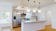 Located at 11 Merrimac Ave in Salt Lake City, Utah, this contemporary multi-floor home offers a thoughtfully designed layout spread across three levels. The main living floor commands the majority of the space and is anchored by a striking open-concept kitchen, dining, and living area. The kitchen is a standout feature, boasting a large central island with a built-in sink, pendant globe lighting, sleek white cabinetry, stainless steel appliances, and a subway tile backsplash — all complemented by warm-toned hardwood flooring that flows throughout. Recessed lighting brightens the generously sized living area, which benefits from multiple windows allowing natural light to pour in. The primary bedroom is well-proportioned, featuring large windows with outdoor views and the same consistent hardwood flooring. Four bathrooms serve the home, including a modern bath with a dual-sink vanity, matte black hardware, and ample cabinetry. Additional practical spaces include a laundry room, pantry, dedicated utility rooms, and multiple closets. The attached garage offers direct interior access and presents a clean, functional footprint. The exterior reflects a polished modern aesthetic with landscaped planters and a welcoming streetside presence in a tree-lined Salt Lake City neighborhood.
