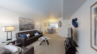This single-floor residence offers a thoughtfully designed layout that maximizes comfort and functionality across its main living areas. The open-concept living room is generously proportioned, featuring plush wall-to-wall carpeting, neutral white walls, and large windows that invite ample natural light. A bold large-format abstract artwork anchors the living space, complemented by a dark leather sofa and glass-top coffee table that lend a contemporary feel.

The adjoining dining area flows seamlessly from the living room and is centered beneath an elegant chandelier, creating a warm, defined space for entertaining. Wainscoting-style wall trim and framed botanical artwork add a refined touch to this area.

The galley-style kitchen is efficiently arranged with white cabinetry, dark granite-style countertops, stainless steel appliances including a refrigerator, range, and microwave, and tile flooring. A decorative runner adds a welcoming element underfoot.

The bedroom is a serene retreat, carpeted and well-lit by a broad window, with ample wall space for artwork and furnishings. The full bathroom features tile flooring, a single vanity with warm-toned countertops, a combined tub and shower, and clean white cabinetry. Throughout, the space maintains a cohesive palette of warm neutrals accented by navy blue tones.