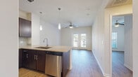 Located in Richmond, TX, this one-bedroom, two-bathroom residence offers a well-designed single-level layout that maximizes functionality and comfort. The open-concept living and kitchen area serves as the heart of the home, featuring warm hardwood-style flooring that flows seamlessly throughout. The kitchen is appointed with rich dark cabinetry, granite-style countertops, a stainless steel appliance suite including a refrigerator, electric range, microwave, and dishwasher, and a peninsula with pendant lighting overhead. A ceiling fan anchors the living area, which is bathed in natural light and opens directly to a private balcony through elegant French doors. A built-in shelving closet near the entry provides convenient storage. The bedroom is a comfortable retreat with a ceiling fan, a large window allowing natural light, and hardwood-style flooring. Two full bathrooms serve the home; one features dark wood cabinetry with a granite-topped vanity, a large mirror, and a tub-shower combination with neutral tile surround and a decorative mosaic accent strip. The overall aesthetic is clean and contemporary, with neutral tones, modern finishes, and a bright, airy atmosphere throughout.