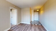 Located at 1650 N Farwell Ave in Milwaukee, WI, this single-floor unit sits in the heart of the city's lively East Side neighborhood. The entry foyer immediately sets a distinctive tone with its bold black-and-white checkered tile flooring and a warm yellow accent wall, illuminated by a pendant light fixture overhead. From the entryway, the layout flows naturally into the main living area, which features durable hardwood-style plank flooring and neutral beige walls that provide a clean, versatile backdrop. A large window in the living area allows ample natural light to fill the room, complemented by a radiator unit for efficient heating. The bedroom is carpeted for comfort and includes a built-in closet with sliding doors and overhead storage, along with a window offering views of the surrounding neighborhood. The bathroom is finished with white ceramic tile flooring and features a vanity with a white cabinet, a toilet, and a tub-shower combination. The kitchen, visible in the floorplan overview, is outfitted with white cabinetry and a functional layout. Throughout the unit, white trim and baseboards provide a crisp contrast to the warm wall tones, creating a cohesive and inviting living environment.
