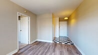 Located at 1650 N Farwell Ave in Milwaukee, WI, this single-floor unit sits in the heart of the city's lively East Side neighborhood. The entry foyer immediately sets a distinctive tone with its bold black-and-white checkered tile flooring and a warm yellow accent wall, illuminated by a pendant light fixture overhead. From the entryway, the layout flows naturally into the main living area, which features durable hardwood-style plank flooring and neutral beige walls that provide a clean, versatile backdrop. A large window in the living area allows ample natural light to fill the room, complemented by a radiator unit for efficient heating. The bedroom is carpeted for comfort and includes a built-in closet with sliding doors and overhead storage, along with a window offering views of the surrounding neighborhood. The bathroom is finished with white ceramic tile flooring and features a vanity with a white cabinet, a toilet, and a tub-shower combination. The kitchen, visible in the floorplan overview, is outfitted with white cabinetry and a functional layout. Throughout the unit, white trim and baseboards provide a crisp contrast to the warm wall tones, creating a cohesive and inviting living environment.