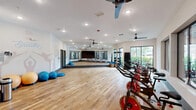 Located at 1348 Passenger St in Chattanooga, TN, this single-floor fitness studio is a thoughtfully designed exercise space that combines functionality with an energizing atmosphere. The studio features warm hardwood flooring throughout, providing a durable and visually appealing surface ideal for a variety of workout activities.

The open layout accommodates a row of spin bikes positioned to face large, bold-framed windows that look into an adjacent weight and strength training area, creating a sense of visual connectivity between workout zones. Natural light filters in through multiple oversized windows, keeping the space bright and inviting.

Full-length mirrors line one wall, amplifying the sense of space and allowing users to monitor their form during exercise. Ceiling fans are strategically installed to maintain airflow and comfort during intense workouts. Recessed lighting ensures consistent illumination throughout.

A standout feature is the motivational wall art — hand-lettered phrases such as "Keep Keepin' On Like a Boss" and "Breathe" are painted directly onto the crisp white walls, accompanied by silhouetted yoga figures, creating an uplifting and dynamic environment. Storage for exercise balls, BOSU trainers, and medicine balls lines the perimeter, keeping the central floor area open and versatile for group classes or individual training sessions.