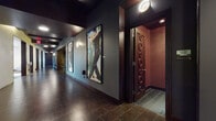 This thoughtfully designed single-floor amenity space offers a rich blend of sophisticated interiors and functional entertainment areas. The entry corridor sets a dramatic tone with dark tile flooring, deep slate-blue walls, and oversized framed artwork lining the walls, leading to a set of distinctive dark wood doors adorned with circular sculptural detailing.

The lounge areas are bright and inviting, featuring floor-to-ceiling windows that frame views of the surrounding cityscape and outdoor greenery. One lounge showcases a bold patterned accent wall, modern upholstered seating, rocking chairs, and gold accent tables, while another offers a more intimate arrangement with leather chairs, a plush sofa, and contemporary artwork.

A dedicated game room includes a full-size billiards table set beneath a striking geometric pendant light, complemented by a wall-mounted television framed by custom teal cabinetry and large windows offering outdoor views.

The kitchen and bar area is equipped with stainless steel appliances, a geometric tile backsplash, pendant lighting, and a long counter lined with teal upholstered bar stools — ideal for social gatherings.

Private screening or media rooms feature deep burgundy walls, plush carpet, and the same signature sculptural wood doors found throughout, creating an intimate and immersive atmosphere. A dedicated art alcove with warm golden lighting and sculptural seating adds a gallery-like focal point to the space.
