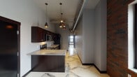 Located at 204 E Grand Ave in downtown Eau Claire, Wisconsin, this single-floor unit blends industrial-chic aesthetics with modern finishes throughout. Striking polished marble-look epoxy floors with bold veining flow seamlessly across every room, creating a cohesive and sophisticated foundation. Exposed cylindrical ductwork runs along the ceilings, complemented by warm copper-toned pendant lighting that adds an inviting contrast to the cool gray walls and dark baseboards.

The kitchen is a standout feature, equipped with rich dark espresso cabinetry reaching toward the elevated ceilings, granite countertops, a central island, and a full suite of stainless steel appliances including a refrigerator, range, microwave, and dishwasher. Multiple pendant lights illuminate the workspace, enhancing both function and style.

The living and bedroom areas are generously proportioned, with large black-framed windows inviting abundant natural light and offering views of the surrounding Eau Claire downtown skyline. The bathrooms continue the refined material palette, featuring granite-topped dark vanities, mirrors, and marble-look flooring. One bathroom includes a walk-in shower. The space also includes a dedicated laundry hookup area, rounding out a thoughtfully designed and well-appointed urban residence.
