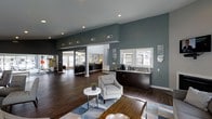 Located at 6200 Riese Dr in Raleigh, NC, this single-floor community space offers a polished, modern environment designed for both comfort and functionality. The open-concept layout connects multiple lounge and activity areas, creating a sense of spaciousness and easy flow throughout.

The main gathering area features rich dark hardwood flooring, high ceilings with recessed lighting, and walls painted in a sophisticated slate-blue tone that lends the space a contemporary, welcoming ambiance. Comfortable seating, including a light gray upholstered armchair and a sleek round side table, invites relaxed conversation or quiet lounging.

A dedicated refreshment station lines one wall, complete with dark cabinetry, a countertop with a sink, and coffee-making amenities — ideal for residents or guests to help themselves. Framed artwork and mirrors add decorative character throughout.

Adjacent rooms are visible through open archways and large windows, including what appears to be a fitness area and a well-lit secondary lounge with ample natural light from floor-to-ceiling windows. The interconnected design ensures each zone feels distinct yet cohesive, making this a versatile, well-appointed community hub.