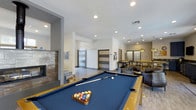 This single-floor amenity space is thoughtfully designed to offer a well-rounded social and recreational experience. At the heart of the room sits a full-size pool table with a classic blue felt surface, making it an immediate focal point for entertainment. The open-concept layout flows seamlessly between distinct activity zones, each defined by modern architectural details including recessed lighting and clean white walls.

A contemporary fireplace with a stone surround anchors one side of the room, adding warmth and a stylish visual element to the lounge area. Nearby, comfortable dark leather seating provides a relaxed setting for conversation or unwinding. Sliding barn-style doors lend an industrial-modern aesthetic while offering flexible room separation.

Toward the back of the space, a dining and bar area is illuminated by pendant lighting, creating an inviting atmosphere for casual meals or social gatherings. The hardwood-style flooring ties the entire space together, contributing to a cohesive and polished look. With its combination of entertainment features, cozy gathering spots, and well-considered design, this amenity space is built to accommodate a variety of social activities in a refined, welcoming environment.