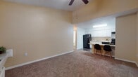 This single-floor residence offers a functional and well-appointed layout designed for comfortable everyday living. The open-concept living area is immediately welcoming, featuring soaring vaulted ceilings, warm neutral-toned walls, and plush carpeted flooring throughout. A ceiling fan provides year-round comfort, and a window near the entry allows natural light to fill the space.

The kitchen is thoughtfully updated, showcasing crisp white cabinetry with brushed nickel hardware, granite-look countertops, a stainless steel double-basin sink, and a distinctive hexagonal tile backsplash. Black appliances, including a refrigerator, range with oven, and range hood, provide a bold contrast to the bright cabinetry. Wood-look flooring in the kitchen adds a clean, durable finish. A curved granite-topped breakfast bar connects the kitchen to the living area and offers seating for casual dining.

The bedroom is generously proportioned with carpeted floors, a ceiling fan, and a built-in closet with wire shelving and bi-fold doors, providing ample storage. The full bathroom features wood-look tile flooring, a white vanity, and a full-size tub-shower combination with clean white surround panels, maintaining a consistent, tidy aesthetic throughout the home.