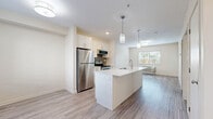 Located at 1469 K.L.O Road in Kelowna, BC, this well-appointed one-bedroom, one-bathroom unit offers a thoughtfully designed open-concept layout filled with natural light. The kitchen is a standout feature, showcasing crisp white cabinetry, a grey tile backsplash, stainless steel appliances including a refrigerator, electric range, and over-the-range microwave, and a sleek white island with a double undermount sink and pendant lighting overhead. The kitchen flows seamlessly into the living area, which is brightened by a window overlooking greenery outside. Light-toned laminate flooring runs throughout the entire unit, lending a cohesive, modern feel. The bedroom is a comfortable and private retreat, featuring a mirrored sliding-door closet with built-in shelving, a window with blinds providing natural light, and baseboard heating. The clean, neutral-toned bathroom includes a vanity with mirror, toilet, and a shower-tub combination. A dedicated laundry room provides added convenience, complete with a hot water tank and overhead shelving. The overall ambiance of the unit is clean, bright, and contemporary, making it a practical and inviting space in a well-situated Kelowna location.