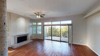 This two-floor residence offers a well-appointed layout with a blend of elegant and functional design elements throughout. The main living area makes a strong impression with warm hardwood flooring, a tiled fireplace flanked by built-in shelving, and a decorative stone column that adds architectural character. Large sliding glass doors open to a balcony, flooding the space with natural light and framing views of mature trees. Clerestory windows above the doors further enhance the brightness of the room. A ceiling fan provides additional comfort.

The kitchen is thoughtfully designed with white shaker cabinetry, dark granite countertops, a subway tile backsplash, and stainless steel appliances including a dishwasher, range, and microwave. A breakfast bar with a curved counter connects the kitchen to the adjoining dining or living space, both finished with hardwood flooring.

Bedrooms are carpeted and feature vaulted ceilings with ceiling fans, walk-in closets with built-in shelving and hanging rods, and sliding glass doors that open to a balcony with outdoor views. Bathrooms include tiled tub-shower combinations with accent tile detailing and tile flooring.