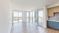 Located in the heart of Los Angeles, this modern 1-bedroom, 1-bathroom residence at 808 S Western Ave offers a thoughtfully designed layout with clean lines and contemporary finishes throughout. Light wood-style flooring flows seamlessly across the entire space, complementing the crisp white walls and creating a bright, cohesive aesthetic.

The open-concept kitchen and living area is a standout highlight, anchored by expansive floor-to-ceiling windows and a glass balcony door that flood the space with abundant natural light and frame sweeping city views. The kitchen is well-appointed with two-tone cabinetry — light wood uppers paired with muted blue-grey lowers — white quartz countertops, a glass tile backsplash, and a full suite of stainless steel appliances including a range, microwave, and refrigerator.

The bedroom is a comfortable, serene retreat with its own large window overlooking the Los Angeles cityscape, providing ample natural light. A dedicated walk-in closet offers generous built-in shelving and dual hanging rods for organized storage.

The bathroom features a modern grey vanity with an undermount sink, a backlit LED mirror, and a tiled shower enclosure, conveying a spa-like feel. The hallways connect the spaces efficiently, completing a functional and stylish urban residence.