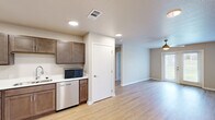Located at 1409 Courtyard Dr SE in Bondurant, Iowa, this well-appointed one-bedroom, one-bathroom unit offers a thoughtfully designed single-floor layout. The open-concept kitchen is a standout feature, showcasing rich dark-stained cabinetry, white countertops, and a full suite of stainless steel appliances including a gas range, dishwasher, refrigerator, and microwave. Light wood-tone LVP flooring flows throughout the main living areas, creating a clean and cohesive aesthetic. The living room is bright and airy, enhanced by a ceiling fan and a glass patio door that invites natural light and opens to an outdoor view of green surroundings. The bedroom features plush carpeting, a ceiling fan, a window overlooking the outdoors, and a reach-in closet with built-in shelving for organized storage. The bathroom is well-equipped with a wide vanity, generous counter space, a large mirror, dark wood cabinetry including a tall linen tower, and LVP flooring. A dedicated laundry area houses a full-size Samsung front-loading washer and dryer with overhead shelving. The unit combines functional design with modern finishes, offering a comfortable and practical living space.