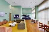 Located at 611 O'Keefe Ave in New Orleans, this single-floor open-plan space combines a living room, dining area, and kitchen in a cohesive, design-forward layout. Soaring ceilings amplify the sense of volume throughout, while mint-green walls lend the interior a calm, contemporary character. Warm hardwood flooring ties all areas together seamlessly.

The living area is anchored by a generous sectional sofa and a pair of blush-pink velvet armchairs arranged on a bold mustard-yellow area rug. A marble-topped coffee table and a wood credenza complete the lounge setting, with curated artwork adorning the tall walls. Floor-to-ceiling sheer curtains line the expansive glazed facade, diffusing abundant natural light across the space and offering views to the outdoors.

The dining zone features multiple mid-century modern wood tables with Danish-style chairs, positioned to take advantage of the natural light from the large windows. A sleek marble-topped table adds an elegant touch.

The kitchen is outfitted with dark cabinetry, granite countertops, professional-grade stainless steel appliances including a gas range with hood, a full-size refrigerator, and a dishwasher. Steel-framed glass partition doors connect the space to an adjacent area, adding an industrial-modern accent to the overall refined aesthetic.
