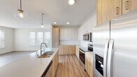 This well-appointed single-floor residence showcases a clean, contemporary design throughout. The open-concept kitchen is a standout feature, combining white upper cabinetry with warm natural wood-toned lower cabinets and a white tile backsplash. A large center island with a undermount sink and pendant globe lighting serves as both a functional workspace and a visual centerpiece. Stainless steel appliances — including a refrigerator with ice and water dispenser, electric range, over-the-range microwave, and dishwasher — complete the kitchen. Light hardwood-style flooring flows seamlessly from the kitchen into the expansive open living area, which is bathed in natural light from large windows. Bedrooms feature plush carpet and generous closet space, including a walk-in closet outfitted with wire shelving systems. The primary bathroom includes a dual-sink vanity with a wide mirror, hardwood-style flooring, a walk-in shower, and ample storage. A secondary bathroom offers a full tub-shower combination. An in-unit laundry room with a full-size washer and dryer adds everyday convenience. Recessed lighting throughout the home enhances the bright, airy ambiance of this thoughtfully designed space.