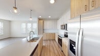 This well-appointed single-floor residence showcases a clean, contemporary design throughout. The open-concept kitchen is a standout feature, combining white upper cabinetry with warm natural wood-toned lower cabinets and a white tile backsplash. A large center island with a undermount sink and pendant globe lighting serves as both a functional workspace and a visual centerpiece. Stainless steel appliances — including a refrigerator with ice and water dispenser, electric range, over-the-range microwave, and dishwasher — complete the kitchen. Light hardwood-style flooring flows seamlessly from the kitchen into the expansive open living area, which is bathed in natural light from large windows. Bedrooms feature plush carpet and generous closet space, including a walk-in closet outfitted with wire shelving systems. The primary bathroom includes a dual-sink vanity with a wide mirror, hardwood-style flooring, a walk-in shower, and ample storage. A secondary bathroom offers a full tub-shower combination. An in-unit laundry room with a full-size washer and dryer adds everyday convenience. Recessed lighting throughout the home enhances the bright, airy ambiance of this thoughtfully designed space.