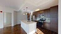 Located at 1 Harbor Point in Stamford, Connecticut, this two-bedroom, two-bathroom residence combines modern design with spectacular waterfront views. The open-concept living area is anchored by rich hardwood flooring and expansive floor-to-ceiling windows that flood the space with natural light while framing sweeping views of the harbor and marina below. The well-appointed kitchen features a large center island with an undermount sink, sleek white quartz countertops, dark wood cabinetry, and a full suite of stainless steel appliances including a gas range, microwave, and refrigerator. Pendant lighting adds a contemporary touch overhead, and an in-unit stacked washer and dryer provides added convenience. The bedrooms are carpeted for comfort, with the primary bedroom offering dramatic floor-to-ceiling windows showcasing breathtaking marina and water views. Both bedrooms include generous closet space with built-in wire shelving systems. The two bathrooms are finished with wood-look tile flooring and dark wood vanities with light countertops. One bathroom features a tub-shower combination, while the second offers a vanity with ample storage. A keypad-secured entry door completes this thoughtfully designed residence.
