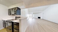 This 810 sq ft single-floor unit offers 2 bedrooms and 2 bathrooms. The bright living room features vaulted ceilings, light hardwood flooring, a wood-burning fireplace with a tile surround, and sliding glass doors providing outdoor access. The galley-style kitchen is equipped with dark cabinetry, white quartz countertops, black appliances, and a peninsula breakfast bar. Both bedrooms feature plush carpet, natural light, baseboard heating, and louvered sliding closet doors. The bathrooms include dark vanities, white quartz countertops, and tiled tub-shower combos with hardwood-style flooring throughout.