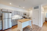 This single-story unit offers a thoughtfully designed layout that maximizes functionality across its well-proportioned floor plan. The interior is finished in a clean, contemporary style with neutral tones and modern fixtures throughout.

The kitchen serves as a standout feature, showcasing grey cabinetry with sleek hardware, a classic white subway tile backsplash, and a full suite of stainless steel appliances including a refrigerator, electric range, microwave, and dishwasher. A mobile kitchen island with a butcher block top provides additional prep and storage space. Wood-look plank flooring ties the kitchen and living areas together cohesively.

The living room benefits from natural light through windows with blinds and includes a door providing exterior access. The space is open and versatile, suitable for a variety of furniture arrangements.

The bedroom features plush carpeting, a ceiling fan, and a walk-in closet equipped with wire shelving systems for organized storage. The full bathroom is finished with grey cabinetry, a marble-look countertop, a large mirror, and a tub-shower combination, all set on wood-look flooring for a clean, cohesive look.