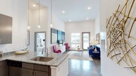 This thoughtfully designed single-floor residence showcases a contemporary aesthetic defined by soaring ceilings and an open, airy layout throughout. Polished concrete floors flow seamlessly through the main living areas, lending an urban, loft-inspired character to the space.

The kitchen is a standout feature, outfitted with rich dark cabinetry, granite countertops, stainless steel appliances — including a refrigerator, range, microwave, and dishwasher — and a generous breakfast bar with seating. Pendant lighting above the island adds a refined finishing touch. The kitchen opens directly into the living and dining area, which benefits from large windows and a glass door that invite abundant natural light and exterior views.

The living area offers a welcoming atmosphere with its dramatic ceiling height and ample space for both lounging and entertaining. A decorative exterior door provides access to the outdoors, further enhancing the sense of openness.

The bedrooms continue the high-ceiling design, each filled with natural light from large windows. The primary suite features an en-suite bathroom with a long granite vanity, dark cabinetry, and wood-look tile flooring. A secondary bathroom includes a granite vanity and a tub-shower combination. Both bathrooms reflect a consistent, polished design language that ties the entire residence together.