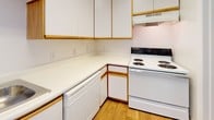 This single-floor residence offers a bright, clean, and functional layout designed for comfortable everyday living. The interior is finished with a neutral white and beige palette throughout, creating a light and airy atmosphere.

The living area features soft wall-to-wall carpeting and multiple windows fitted with blinds, allowing natural light to fill the room. It connects seamlessly to the dining area, which is finished with warm wood-tone laminate flooring that extends into the kitchen.

The kitchen is efficiently laid out in an L-shape configuration, offering ample counter space with white laminate countertops, white cabinetry accented with wood-tone trim, and a full suite of white appliances including a coil-top electric range, dishwasher, and refrigerator. A built-in range hood is positioned above the stove for ventilation.

Two full bathrooms are included, each featuring a tub-shower combination, toilet, and a vanity with white cabinetry and wood-tone accents. Wood-tone flooring and a large mirror complete the practical and clean aesthetic.

The bedrooms are carpeted and well-sized, each with windows providing natural light. Generous closet space is available, including a wide closet with a full-length hanging rod. The overall design is simple, functional, and move-in ready.