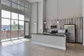 Located at 120 W Trinity Place in Decatur, Georgia, this two-story residence showcases a modern design defined by dramatic double-height ceilings and an open, airy layout. The main level centers on a spacious open-concept living and kitchen area, where soaring ceilings create a striking sense of volume. The kitchen features a large island with a dark countertop, textured wood-toned cabinetry, stainless steel appliances, a tile backsplash, and pendant lighting suspended from above. Light wood-style flooring extends throughout the main living area, complementing the neutral palette. A set of French doors opens to an additional flexible room on this level. Floor-to-ceiling windows along one wall flood the space with abundant natural light and provide views of the surrounding brick exterior.

The upper level offers carpeted bedrooms with ceiling fans and interior windows that overlook the double-height main living area below, reinforcing the home's open, connected feel. One bedroom includes a closet accessed through a panel-style door. Two bathrooms serve the residence: the primary bath features a dual-sink vanity with dark countertops, white cabinetry, a large framed mirror, and a glass-enclosed shower, while the secondary bath includes a tub-shower combination and matching finishes.