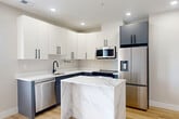 Located at 2385 Rhode Island Ave NE in Washington, DC, this thoughtfully designed 2-bedroom, 2-bathroom unit offers a contemporary living experience with modern finishes throughout. The open-concept kitchen serves as a centerpiece, featuring a striking marble-finish island, two-tone cabinetry with crisp white upper cabinets and slate-blue lower cabinets, matte black hardware, and a full suite of stainless steel appliances. Light-toned hardwood flooring runs seamlessly throughout the entire unit, enhancing the bright, airy atmosphere created by recessed lighting and neutral wall tones. The primary bedroom offers a comfortable footprint with a sliding glass door that opens to an outdoor view, filling the room with natural light. The second bedroom includes a double-door closet, providing ample storage. Both bedrooms are served by well-appointed bathrooms — one featuring a glass-enclosed walk-in shower with marble-style wall tiles, wood-look tile flooring, and matte black fixtures, while the second bathroom offers a clean, functional design. A dedicated utility room adds practical convenience. The unit also benefits from an exterior deck visible from the building's exterior, contributing to an overall modern and functional urban living environment.