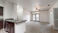 Located at 15330 Liberty River Dr in Houston, TX, this single-floor residence offers a well-designed, open-concept layout with a clean, neutral aesthetic throughout. The spacious living area is finished with plush carpeting, crown molding, and a ceiling fan, while French doors topped with transom windows invite abundant natural light and provide access to a private balcony with outdoor views.

The kitchen is a functional highlight, featuring rich dark wood cabinetry, granite-style countertops, a breakfast bar peninsula with a double stainless steel sink, and a full suite of stainless steel appliances including a refrigerator with ice maker, a range, a microwave, and a dishwasher. Light wood-style flooring runs through the kitchen, contrasting beautifully with the cabinetry.

The bedrooms are generously sized, each finished with soft carpeting and ample natural light from well-positioned windows. Crown molding adds a refined touch throughout. The primary bathroom features a dual-sink vanity with dark wood cabinetry and stone-style countertops, complemented by a full tiled tub and shower surround. A dedicated hallway connects the living spaces to the private quarters, completing this thoughtfully laid-out home.
