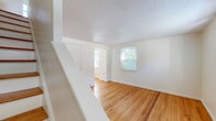 Located at 6A Weis Rd in Albany, NY, this 2-bedroom, 1-bathroom home spans three floors, offering a well-organized and functional layout throughout. The main level features a bright living room with warm hardwood flooring, white walls, and a front entry door with a transom window that allows natural light to fill the space. A staircase leads to the upper levels, maintaining a clean, open feel. The kitchen is equipped with white cabinetry, dark laminate countertops, a gas range, and a double basin sink beneath a window overlooking the outdoors. An adjoining dining room completes the main living area. Upstairs, two bedrooms continue the hardwood flooring theme. The primary bedroom includes a closet and benefits from multiple windows that bring in generous natural light and views of the surrounding greenery. The second bedroom is compact yet functional. The full bathroom showcases classic tilework with a black-and-navy accent border, a checkerboard mosaic tile floor, a pedestal-style vanity, and a tub-shower combination with a window above. The basement level provides unfinished utility space, housing the water heater and offering additional storage potential. Textured ceilings are present throughout the upper floors, adding a traditional character to the home.