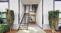 This contemporary apartment complex in Atlanta showcases a harmonious blend of urban convenience and natural beauty. The buildings feature a clean, modern aesthetic with predominantly white exteriors accented by blue lower levels. Large windows and private balconies characterize the facade, offering residents ample natural light and outdoor space.

The property's landscaping is a standout feature, with mature trees providing shade and a sense of established greenery. A community garden area, rich with diverse plantings in various containers, adds a vibrant touch of nature and offers residents a space for gardening and relaxation.

Well-maintained pathways guide residents through the complex, including a notable covered walkway with an arched entrance. The grounds include both grassy areas and decorative stone elements, creating visual interest and texture.

Parking appears to be conveniently available, with spaces close to the buildings. The complex's design prioritizes pedestrian-friendly spaces, with wide sidewalks and communal areas that encourage a sense of community.

The architecture emphasizes vertical lines, seen in the siding details and stairway structures, which add a modern flair to the overall design. This thoughtful blend of style, nature, and community amenities creates an inviting living environment in the heart of Atlanta.