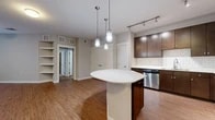 This thoughtfully designed two-bedroom, one-bathroom residence offers a comfortable and efficient single-level layout. The kitchen serves as a standout feature, showcasing rich dark wood cabinetry, a classic white subway tile backsplash, stainless steel appliances including a refrigerator, range, microwave, and dishwasher, and a large center island with a light quartz countertop. Pendant lighting and a track lighting system illuminate the space stylishly, while warm hardwood-style flooring extends throughout the kitchen and main living areas. A hallway connects the main living space to the private quarters, where both bedrooms are finished with plush wall-to-wall carpet, ceiling fans, and windows that invite natural light. The primary bedroom offers a comfortable footprint with outdoor tree views. The bathroom features hardwood-style tile flooring, a tub-shower combination, and direct access to a dedicated closet with built-in shelving for ample storage. Neutral wall tones throughout create a clean, versatile backdrop. The layout flows logically from the open kitchen and living area through the hallway to the bedrooms and bathroom, making efficient use of every square foot in this well-organized residence.