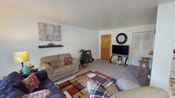 This single-floor home offers a practical and comfortable layout across several well-defined living spaces. The living room is generously sized, featuring soft carpeting, a textured ceiling, and room for multiple seating arrangements. A sliding glass door brings in natural light and connects the space to the outdoors, while a ceiling fan adds to the room's functionality. Adjacent to the living area is a dedicated dining space with room for a table and chairs, creating a natural flow for daily living.

The kitchen is efficiently designed with rich dark wood cabinetry that extends to the upper walls, providing ample storage. It includes a full suite of white appliances — refrigerator, electric range, and under-cabinet ventilation — along with tile flooring and a tiled backsplash.

The home includes multiple bedrooms, each carpeted and finished with textured ceilings. The primary bedroom features a window for natural light and a built-in closet with louvered doors and shelving. A secondary bedroom is thoughtfully appointed with a window, closet storage, and a bright, cheerful character. The full bathroom includes tile flooring, a vanity with storage, and a shower-tub combination with a curtain enclosure. Overall, the home presents a cozy and livable environment throughout.