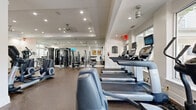 Located at 625 Cameron Walk Ct in Charlotte, NC, this fitness center offers a comprehensive and well-appointed workout facility across a single floor. The space is thoughtfully divided into distinct exercise zones, providing a full range of fitness options for users of all levels.

The cardio area is lined with treadmills and elliptical trainers, each equipped with individual screens for entertainment during workouts. Large floor-to-ceiling windows along one wall flood the area with natural light and offer pleasant views of the surrounding greenery, creating an energizing atmosphere. Ceiling fans provide additional airflow and comfort throughout the space.

The strength training zone features a robust selection of cable machines, weight benches, and a dedicated free weights section with a full dumbbell rack. Floor-to-ceiling mirrors line the walls, visually expanding the space and allowing users to monitor their form. Durable rubber flooring throughout provides both safety and comfort.

A separate alcove-style area houses stationary bikes and additional cycling equipment, accented by a decorative aquarium wall display that adds a calming, unique visual element. Recessed lighting and tray ceilings in select areas add an upscale architectural touch. The overall ambiance is clean, bright, and modern, making this fitness center a functional and inviting amenity.