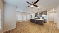 This well-appointed single-floor residence showcases a thoughtfully designed open-concept layout that seamlessly connects the living, dining, and kitchen areas. Warm wood-look flooring extends throughout the main living spaces, complemented by neutral tones that create a bright and welcoming atmosphere. Multiple windows dressed with white horizontal blinds invite abundant natural light into the living area, which is topped by a ceiling fan for added comfort.

The kitchen is a standout feature, boasting rich dark-espresso cabinetry, a large central island with a crisp white countertop, and a full suite of stainless steel appliances including a French door refrigerator, range, and microwave. Elegant pendant lighting above the island adds a refined touch, while a tile backsplash ties the space together.

The bedroom offers generous proportions, highlighted by elevated ceilings and direct access to a walk-in closet. The primary bathroom features neutral tile flooring, white shaker-style cabinetry, a quartz vanity with a backlit mirror, and a dedicated walk-in closet. A secondary bathroom provides a full tub-shower combination with crisp white tile surround and matching white cabinetry. The entryway is clean and functional, with panel-style doors and additional storage access rounding out this move-in ready residence.