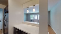 This single-floor residence offers a thoughtfully designed layout with consistent finishes throughout. The kitchen is outfitted with dark espresso cabinetry, light stone countertops, and a full suite of stainless steel appliances, including a dishwasher, range, microwave, and refrigerator. A pass-through counter with pendant lighting connects the kitchen to the adjacent living area, creating an open, communicative flow between spaces. The living and dining areas feature warm hardwood flooring that extends throughout the unit, complemented by soft gray-blue walls that lend a calm, neutral palette. Multiple windows allow natural light to fill these areas, and a set of exterior doors provides direct outdoor access. The bedrooms continue the hardwood flooring and include baseboard heating units beneath the windows. One bedroom offers added functionality with access to a dedicated storage or walk-in closet area. The bathroom is finished with clean white subway tile surrounding a tub-shower combination, fitted with brushed nickel fixtures. Baseboard heating is present throughout, and the overall aesthetic is clean, modern, and move-in ready.
