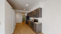 Located at 8220 SE 6th Ave in Portland, Oregon, this single-floor unit offers a clean, modern aesthetic throughout. The galley-style kitchen is a standout feature, showcasing dark walnut-toned cabinetry extending from floor to ceiling, complemented by light quartz countertops and a classic white subway tile backsplash. Stainless steel appliances — including a refrigerator, electric range, built-in microwave, and dishwasher — provide a fully equipped cooking space. Light wood-tone flooring runs continuously throughout the unit, lending warmth and visual continuity. A barn-style sliding door adds a contemporary architectural detail near the kitchen entry. The bathroom is finished in a clean, minimal style with matching dark wood cabinetry, a quartz vanity top, a large wall mirror, and a full tub/shower combination with a curved curtain rod. The bedroom is a bright, open room with white walls, hardwood-style flooring, and a sliding-door closet with built-in shelving and hanging rods, offering practical storage. Recessed lighting throughout the unit ensures consistent, comfortable illumination. The overall design emphasizes modern simplicity, functional layouts, and cohesive finishes across all spaces.