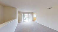 This single-floor residence offers a well-organized layout designed for practical, comfortable living. The spacious living area is finished with neutral-toned carpeting and bathed in natural light through a large sliding glass door, which provides direct outdoor access and views of the surrounding neighborhood. A half-wall partition adds subtle architectural definition to the space, separating it from adjacent areas while maintaining an open feel.

The bedrooms are carpeted and feature vertical blinds over windows that allow natural light to filter through. One bedroom includes a connecting door leading to a bathroom, suggesting an en-suite configuration. Additional bedrooms are generously sized with multiple ventilation registers and ample wall space.

The kitchen runs galley-style with warm-toned wood cabinetry, laminate countertops, a double sink, and a full suite of appliances including a refrigerator, electric range, microwave, and dishwasher. Wood-look vinyl flooring extends through the kitchen and into a dedicated laundry area, which houses a washer and dryer alongside the HVAC unit and electrical panel.

The bathroom is equipped with a single-sink vanity featuring white cabinetry, a bathtub with shower, and a window with vertical blinds providing natural ventilation.