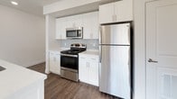 This well-appointed single-floor unit showcases a clean, modern design with a neutral color palette and wood-look flooring that flows through the main living areas. The open-concept kitchen is a standout feature, equipped with stainless steel appliances including a refrigerator, range, and microwave, complemented by crisp white cabinetry, a subway tile backsplash, and a large white quartz island with an integrated sink and pendant lighting overhead. Recessed lighting and direct access to the entryway make this space both functional and welcoming. The living and dining area benefits from abundant natural light, with vertical blinds framing a sliding door that opens to views of surrounding mountains and greenery, alongside an elegant chandelier overhead. Two bedrooms offer plush carpeting, ceiling fans or flush-mount lighting, and windows with urban views of the surrounding neighborhood. The primary bathroom is generously sized, featuring a long white vanity with dual sinks, wood-look flooring, and a walk-in closet with built-in shelving. A second full bathroom includes a tub-shower combination with white tile surround and brushed nickel fixtures. Throughout the unit, consistent finishes and bright, open spaces create a cohesive and inviting living environment.