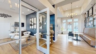 This thoughtfully designed single-floor clubhouse combines contemporary aesthetics with functional communal spaces, creating an inviting environment for residents and guests alike. Light hardwood flooring flows throughout, unifying the open-concept layout under soaring ceilings accented by a statement chandelier near the entrance.

At the heart of the space, a spacious lounge area offers comfortable seating arrangements with mid-century modern furnishings, a wall-mounted television, and curated décor including sculptural accents and lush greenery. Large glass folding doors connect this living area directly to an outdoor pool deck, flooding the interior with natural light and providing seamless indoor-outdoor living.

Glass-walled private meeting rooms offer a transparent yet distinct separation from the main lounge, featuring bold navy blue accent walls, abstract artwork, and dedicated seating — ideal for focused gatherings or private consultations. A café-style kitchen stands out with a striking natural stone tile feature wall framed by arched windows, white shaker cabinetry, a quartz-topped island with bar seating, and stainless steel appliances.

A casual dining nook with leather banquette seating and a decorative arched display cabinet adds warmth and character. Restrooms and a water station are conveniently accessible, rounding out this well-appointed communal facility.