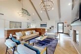 Located at 8365 Dix Ellis Trail in Jacksonville, FL, this thoughtfully designed single-floor amenity space offers a compelling blend of modern aesthetics and functional versatility. The architecture is immediately defined by dramatic vaulted ceilings with exposed wood beams that soar overhead, creating an expansive, airy atmosphere throughout.

The entry area features a sleek wood-paneled reception desk, light tile flooring, and clean white walls, setting a polished, welcoming tone. Adjacent to the entry, a well-appointed kitchenette presents an extended run of white cabinetry with integrated appliances, complemented by decorative artwork and accent pieces.

The central lounge is the heart of the space, anchored by a bold herringbone-patterned hardwood floor and a deep blue area rug. Comfortable contemporary seating — including a neutral sofa, lounge chairs with wood frames, and a sleek coffee table — surrounds a modern fireplace clad in tile, with a wall-mounted flat-screen television above. Statement chandeliers and pendant lighting add a refined, upscale ambiance.

A bright game room wing benefits from a wall of large windows framing lush greenery, filling the space with natural light. A full-size shuffleboard table and additional seating make this area ideal for recreation and socializing. Throughout, the design balances warm wood tones, crisp whites, and contemporary finishes to create an inviting, multi-purpose communal environment.
