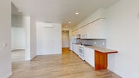 This thoughtfully designed 3-bedroom, 1-bathroom unit offers a clean, modern aesthetic throughout its single-floor layout. Light hardwood-style flooring flows continuously across every room, creating a cohesive and airy feel. The combined kitchen and living area serves as the heart of the unit, featuring a sleek galley-style kitchen outfitted with white flat-front cabinetry extending to the ceiling, a mosaic tile backsplash, neutral laminate countertops, and a full suite of white appliances including a range, built-in microwave, dishwasher, and refrigerator. A wall-mounted mini-split system provides efficient climate control in the living area. A dedicated laundry closet with stacked washer and dryer adds everyday convenience. The three bedrooms are bright and well-proportioned, each finished with crisp white walls and large windows that frame views of surrounding greenery and the urban skyline beyond. The primary bedroom offers a comfortable footprint with ample natural light. The full bathroom features a clean, minimalist design with a tub/shower combination and hardwood-style flooring. Throughout the unit, recessed lighting and a neutral color palette contribute to a fresh, move-in-ready atmosphere.