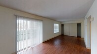 Located on Moore Avenue in Portland, Texas, this single-story unit offers a straightforward, functional layout with consistent finishes throughout. The living area is generously proportioned, featuring warm wood-look laminate flooring and neutral cream-toned walls that create a clean, versatile backdrop. Large vertical blinds cover a full-height sliding glass door, allowing abundant natural light to filter into the space while providing direct outdoor access. A secondary window further brightens the room, and a sizable closet with sliding doors offers notable built-in storage.

The kitchen follows a compact galley configuration, lined on both sides with warm-toned wooden cabinetry and granite-style laminate countertops. A stainless steel sink, white range, and refrigerator complete the functional setup, with light wood-look flooring continuing from the adjacent living space. The kitchen opens visibly from the main living area, maintaining an easy flow between the two spaces.

The bathroom is finished with tile flooring and features a wooden vanity with a granite-style countertop, a large mirror with overhead lighting, and a tiled tub and shower combination. A textured ceiling is present throughout the unit, contributing a consistent architectural character. Overall, the space presents a practical and well-maintained interior suited for comfortable everyday living.