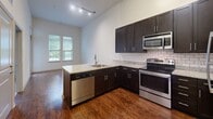 Located at 322 Baldwin Road in Odenton, Maryland, this single-floor 1-bedroom, 1-bathroom residence offers a thoughtfully designed layout that maximizes functionality and comfort. The open-concept kitchen and living area serves as the heart of the home, featuring rich hardwood-style flooring, dark espresso cabinetry, granite countertops, a subway tile backsplash, and a full suite of stainless steel appliances including a range, microwave, dishwasher, and refrigerator. A peninsula with a sink enhances the kitchen's usability while maintaining an open flow into the living space, which is brightened by natural light from a window overlooking the outdoors. The spacious bedroom is finished with plush carpeting and features tall ceilings that lend an airy feel, along with two large windows that invite abundant natural light and views of the surrounding greenery. A dedicated closet provides ample storage. The bathroom is finished with neutral tile flooring, a tiled tub/shower surround, a dark-cabinetry vanity with granite countertop, and clean, modern fixtures. Additional conveniences include an in-unit laundry area and a utility room, rounding out this efficiently designed and move-in-ready residence.