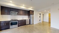 This single-floor unit offers a thoughtfully designed layout that maximizes functionality within a compact footprint. Polished concrete floors run continuously throughout the space, lending an industrial-modern aesthetic that ties all areas together cohesively. Recessed lighting illuminates the interior, complementing the natural light that enters through windows and a glass-panel exterior door.

The kitchen is a standout feature, outfitted with dark espresso cabinetry extending to the ceiling for ample storage, a white tile backsplash, light stone countertops, and a full suite of stainless steel appliances including a range, microwave, dishwasher, and refrigerator. A dedicated in-unit laundry area accommodates a stacked washer and dryer, adding practical convenience.

The living area provides an open, flexible space with clean white walls and a window that brings in natural light and outdoor views. The bathroom features a dark wood vanity with stone countertops, an undermount sink, a large mirror, and chrome fixtures, maintaining the modern aesthetic seen throughout.

Overall, the unit presents a clean, contemporary environment with consistent finishes and efficient use of space.