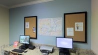 This single-floor professional office space is thoughtfully laid out to support a productive work environment. The interior features light blue walls accented by crown molding, lending the space a clean and polished appearance. Workstations are equipped with desktop computers and printers set atop granite-style countertops, providing ample surface area for daily tasks. Two large cork bulletin boards with black frames are mounted prominently on the wall, serving as practical displays for notices, documents, and reference materials. A detailed map of Benton, Tennessee and its vicinity is centered between the boards, suggesting the office has a local operational or service focus. The overall ambiance is functional and organized, with a layout designed to facilitate workflow and easy access to information. The neutral color palette and tidy arrangement contribute to a calm, professional atmosphere suited for client-facing or administrative operations.